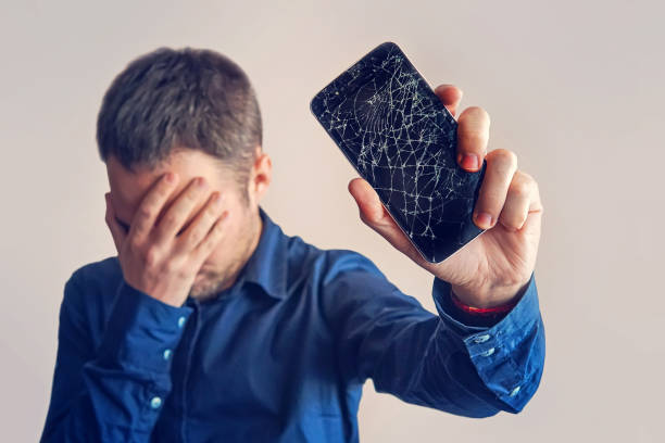 the guy is holding a black smartphone with a broken display. - fracture imagens e fotografias de stock