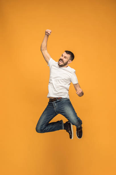 istock Freedom in moving. handsome young man jumping against orange background 959923776