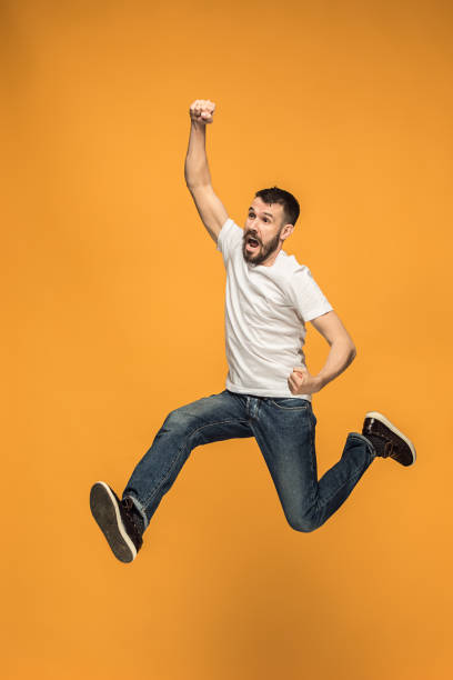 istock Freedom in moving. handsome young man jumping against orange background 959923796