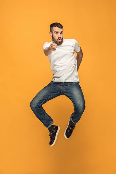 liberté de déplacement. beau jeune homme sauter sur fond orange - fashionable studio shot indoors lifestyles photos et images de collection