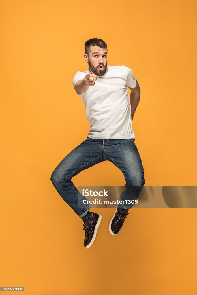 Freedom in moving. handsome young man jumping against orange background Freedom in moving. Mid-air shot of handsome happy young man jumping and gesturing against orange studio background. Runnin guy in motion or movement. Human emotions and facial expressions concept Men Stock Photo