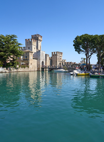 The Scaliger Castle situated at Lake Garda with small boats and tourists.