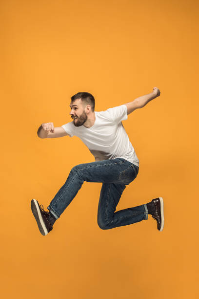 istock Freedom in moving. handsome young man jumping against orange background 959924296