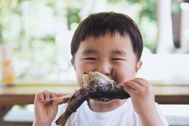 An asian boy eating a trout which he caught in the mountain.