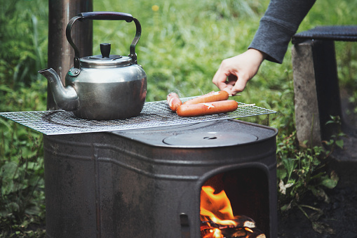 A hand of woman grilling sausages with outdoor oven at camping site.