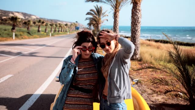 Women standing by convertible car at palm tree seaside highway