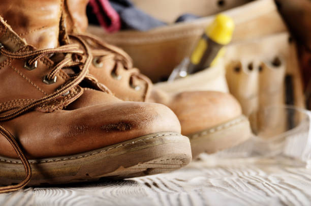 istock Yellow leather used work boots and tool belt on wooden background closeup. Place for text 959934156