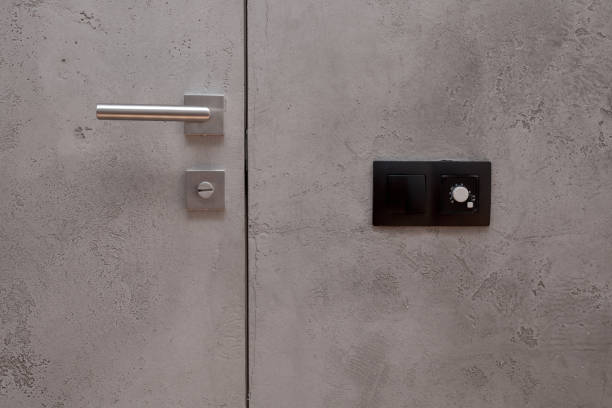 istock Light switch on the gray textured wall next to the door with metallic handle. Wall temperature regulator located near the door to the room 959951254