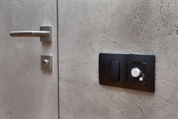 istock Light switch on the gray textured wall next to the door with metallic handle. Wall temperature regulator located near the door to the room 959951836