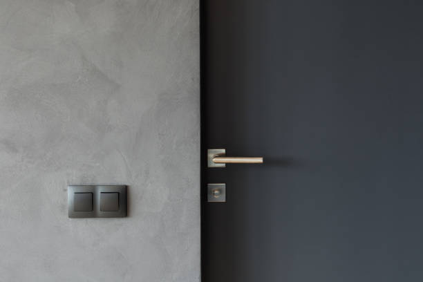 Light switch on the gray textured wall next to the door with metallic handle