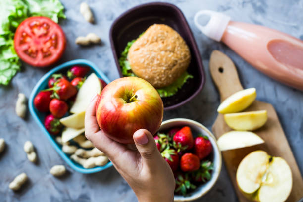 gotowanie obiadu dla dziecka do szkoły. na szarym stole kuchennym. kanapka, truskawki i orzeszki ziemne w lunchboxach. widok z góry. kobieta trzymająca jabłko - school lunch lunch child healthy eating zdjęcia i obrazy z banku zdjęć