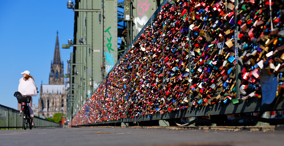 Cologne, Germany - May 06, 2018. Hundreds of thousands love locks mounted at the railing of the Hohenzollern Bridge - accumulated over many years. Woman on a bicycle passing by.
