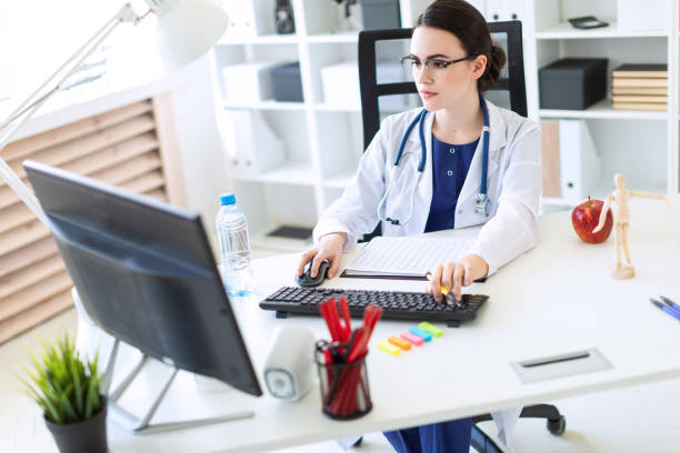 une belle jeune fille dans une robe blanche est assis à un bureau d’ordinateur avec des documents et un stylo dans ses mains. - patient hospital doctor nurse photos et images de collection