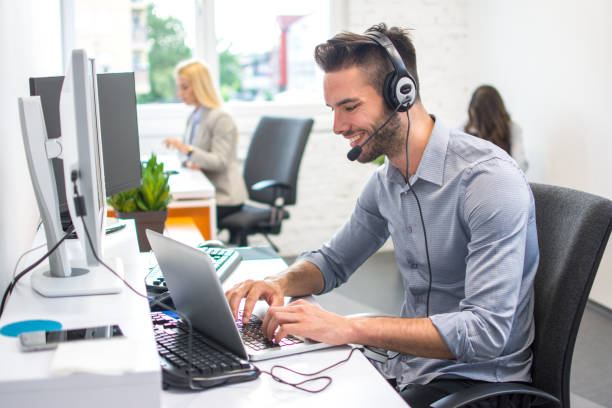 istock Beautiful smiling young man working in call center. Customer support operator with headset working on laptop in office. 959965152