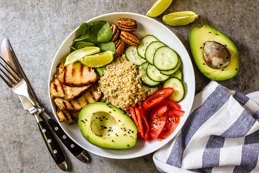 Healthy salad bowl with quinoa, tomatoes, chicken, avocado, and spinach on concrete background top view.