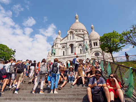 PARIS, FRANCE - MAY 9, 2018: Students and tourists sit on the steps in front of the iconic Sacre Coeur Basilica, Montmarte, on a clear day. Travel and historical landmarks editorial.