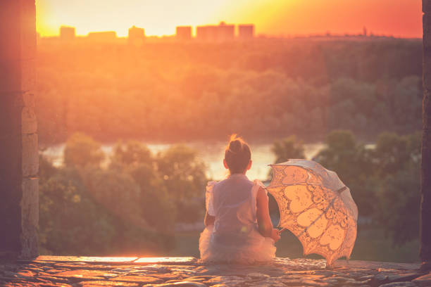 Beautiful little princess with sunshade enjoying at sunset