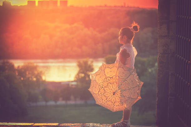 Beautiful little princess with sunshade enjoying at sunset on the Kalemegdan fortress in Belgrade, Serbia