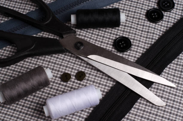 Tools and accessories for sewing. Sewing thread, scissors, buttons, zipper on gray textile background. Close up