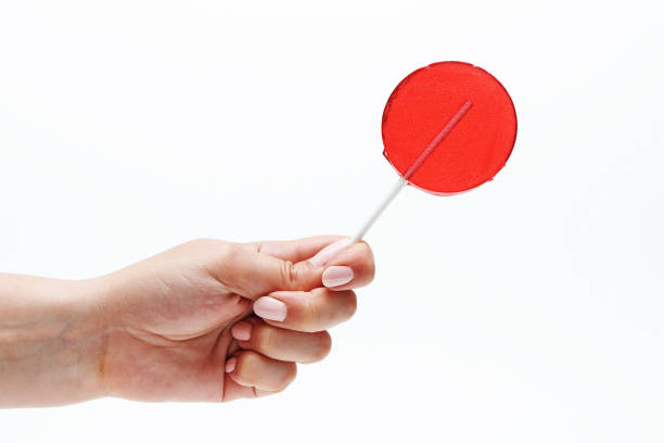 Red round lollipop on a stick in a hand on a white background.