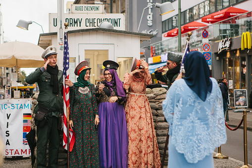 Berlin, October 1, 2017: Positive peaceful cheerful beautiful Arab women in traditional costumes communicate and take pictures with American soldiers next to checkpoint Charlie