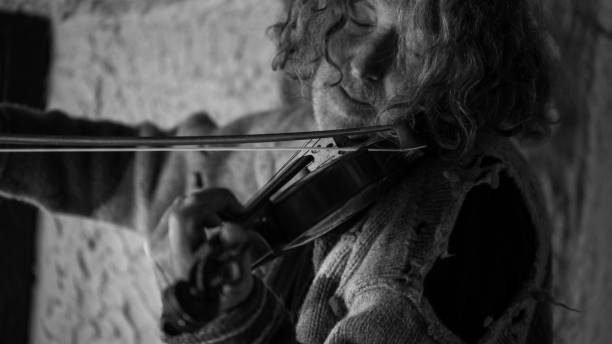 istock Man with long hair and beard in old torn sweater playing a violin 960013514