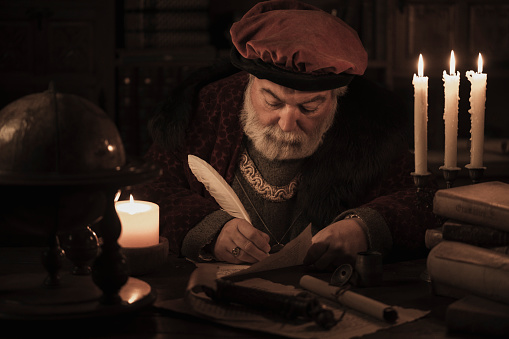 Senior scribe  writing with feather pen on parchment in old library