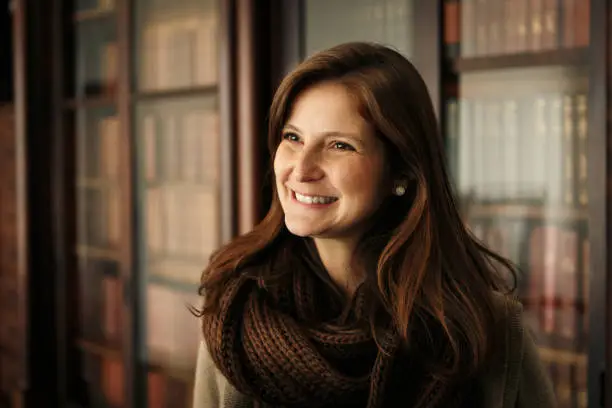 Photo of Smart smiling woman portrait with shelves of books in the background