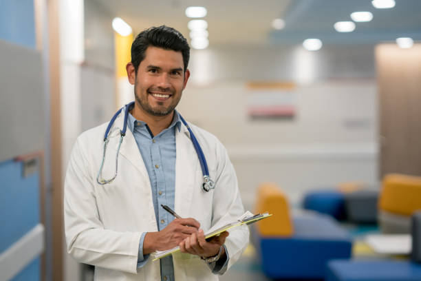 istock Handsome male doctor writing on a medical chart while looking at camera smiling very happy 960073208