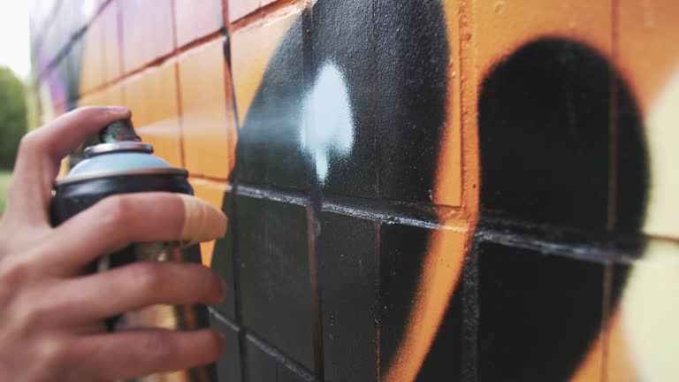 Young man graffiti artist painting on the wall, close up, slow motion