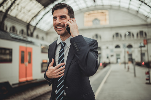 Handsome businessman in suit on train station, using smart phone.