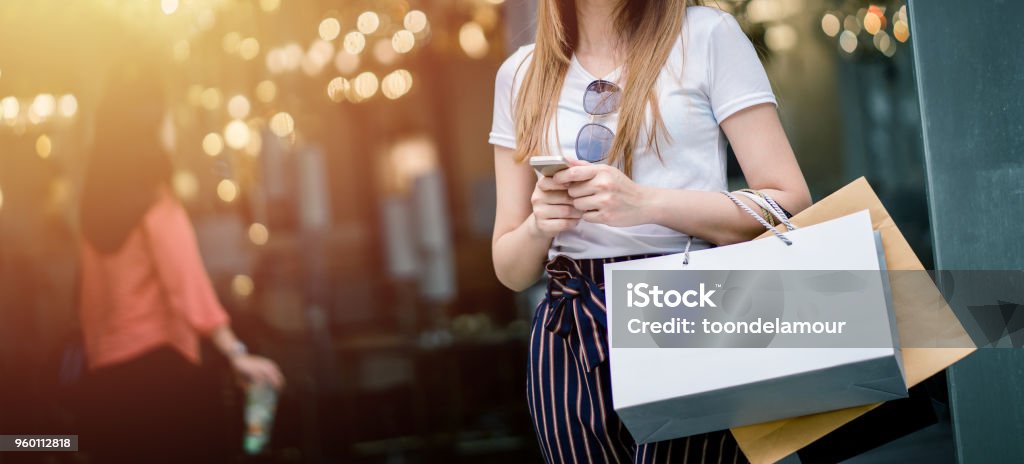 Beautiful girl long hair She is happily shopping at the street mall, She holds several bags of paper and mobile phone, Light bokeh copy space the photo. Retail Stock Photo