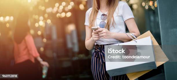 Beautiful Girl Long Hair She Is Happily Shopping At The Street Mall She Holds Several Bags Of Paper And Mobile Phone Light Bokeh Copy Space The Photo Stock Photo - Download Image Now