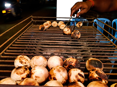 litti, a common north indian food is being baked road side on a coal grill by vendor with white mockup ad space in the background