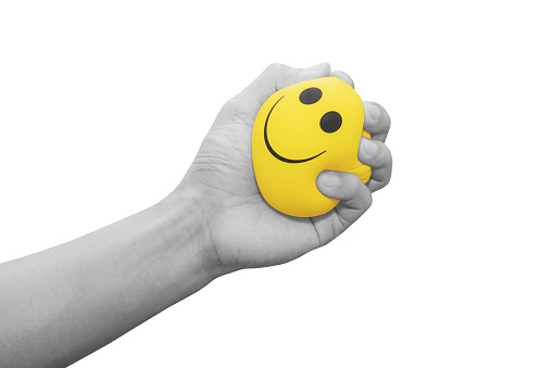 Hand squeezing smiling face yellow stress ball, isolated on white background