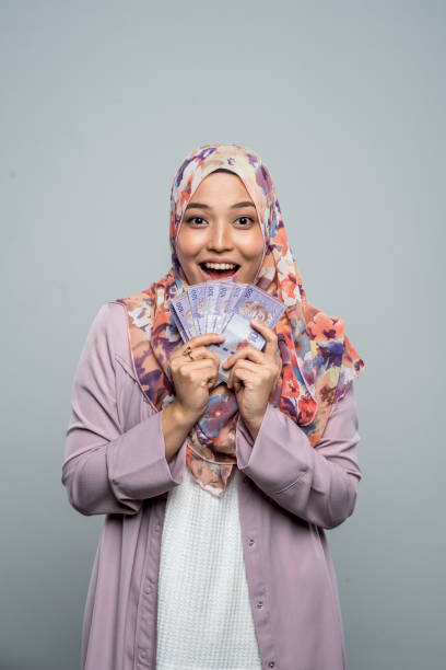 giovane donna malese eccitata che indossa un hijab holding malaysian ringgit cash money - malaysian ringgit foto e immagini stock