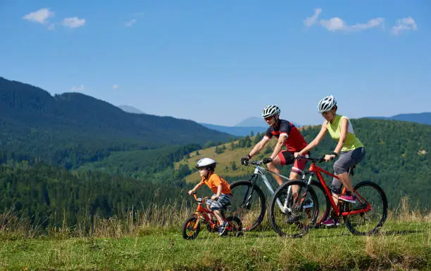 Photo of Family tourists bikers, mom, dad and child riding on bicycles on grassy hill