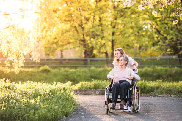 abuela anciana en silla de ruedas con nieta en la naturaleza de la primavera. - silla de ruedas fotografías e imágenes de stock