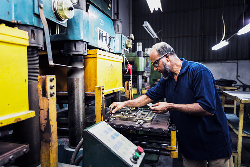 Factory employee adding raw materials to the heavy machinery to continue the production process.