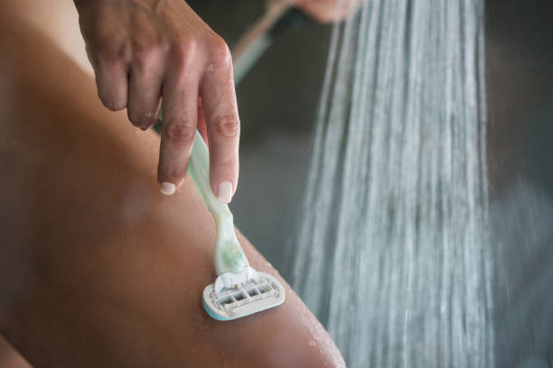 cerca de irreconocible mujer afeitando su muslo bajo la ducha. - wet shave fotografías e imágenes de stock
