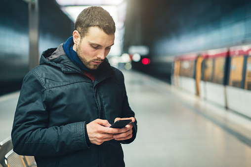 Young adult Caucasian man using his mobile phone in the metro station.