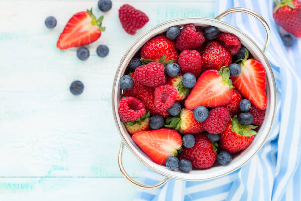 Strawberries, raspberries and blueberries in a colander stock photo