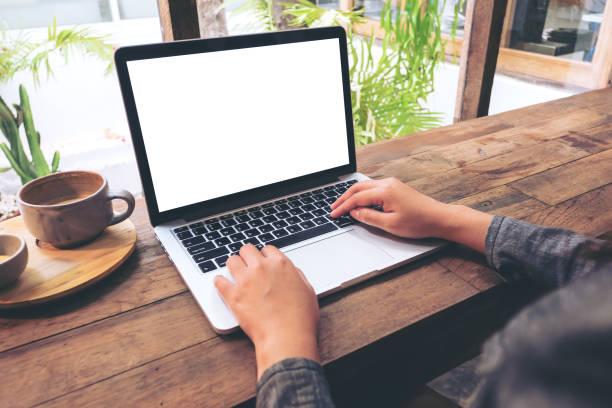 Mockup image of hands using laptop with blank white screen on vintage wooden table in cafe