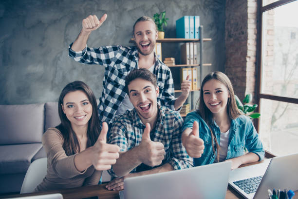 istock Portrait of four young, happy workers in the workplace, workstation using electronic devices, showing thumbs up 960167410