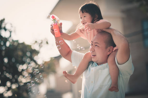 famille chinoise asiatique s’amuser de temps devant leur père de maison ayant fille par-dessus son épaule de liaison - bubble wand child outdoors bubble photos et images de collection