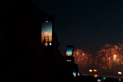 People photographing fireworks celebration with phone. Focus is on smart phone