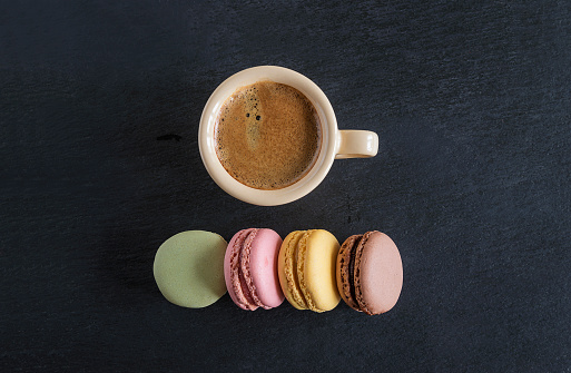Cup of espresso coffee and rang of french macaroons on black slate background with copy space