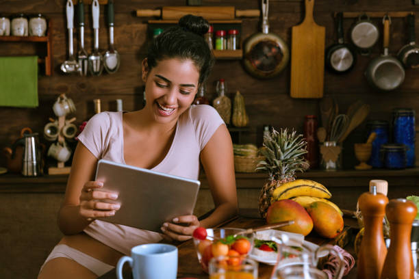istock Happy Hispanic young woman in underwear working in the kitchen and using note book at home office 960214230