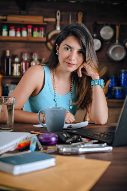istock Confident Hispanic young woman working in the kitchen and using laptop at home office 960216722
