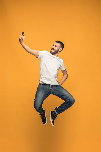 Time to take selfie. Full length of handsome young man taking selfie while jumping